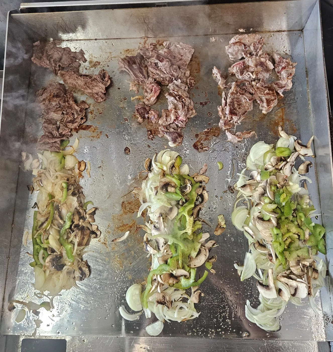 Steak, oignons, champignons et piments sur la plaque